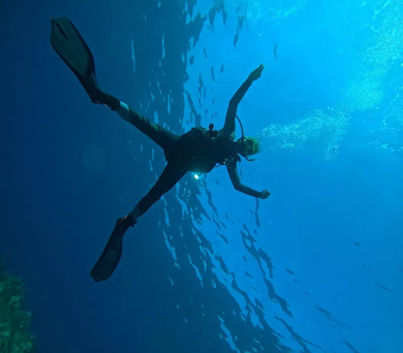 Plongeur en position horizontale, bras ouverts, dans une eau bleue claire