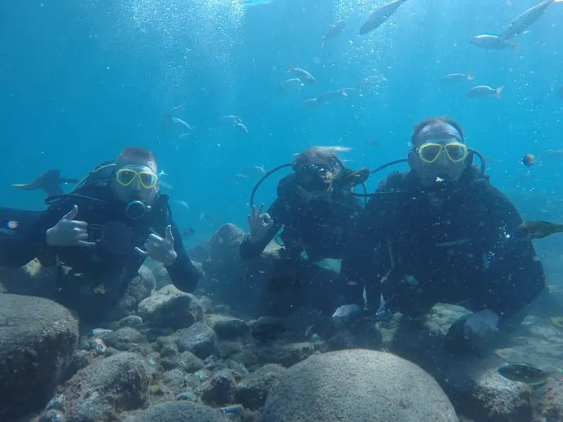 Trois plongeurs souriants font des signes avec leurs mains sous l'eau