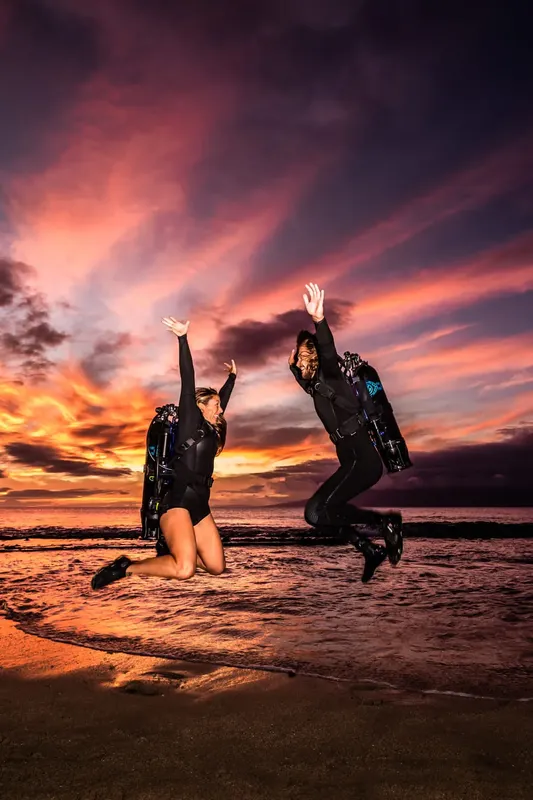 Deux plongeuses sautent sur une plage au coucher du soleil