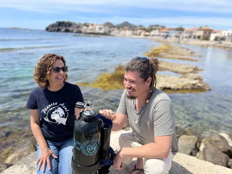 Deux personnes souriantes posent avec une bouteille de plongée en bord de mer