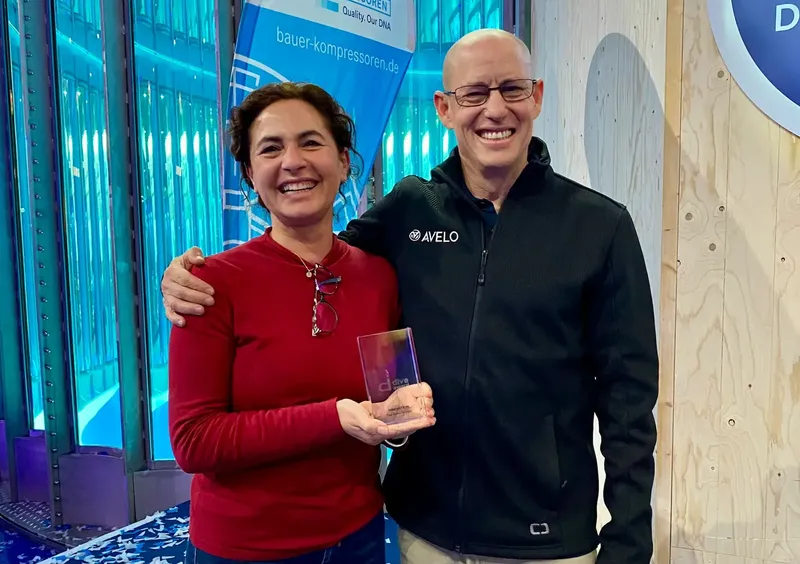 Deux personnes souriantes posent avec un trophée devant un mur bleu