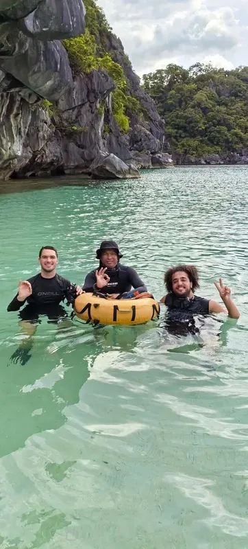 Trois personnes souriantes en combinaison de plongée dans une eau turquoise