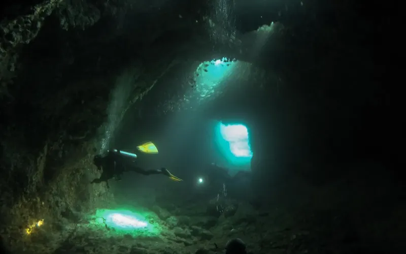 Plongeur explorant une grotte sous-marine avec des rayons de lumière