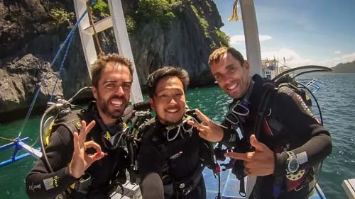 Trois plongeurs souriants sur un bateau avec leur équipement complet