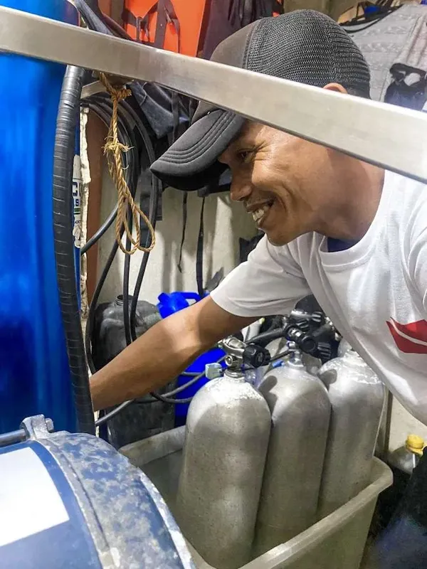 Homme souriant manipulant des bouteilles de plongée et du matériel