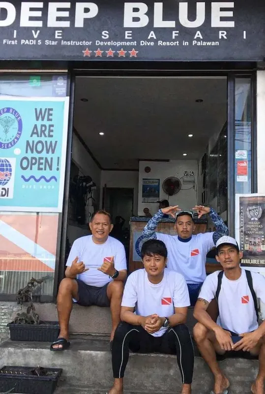 Quatre personnes souriantes devant la devanture d'un centre de plongée ouvert