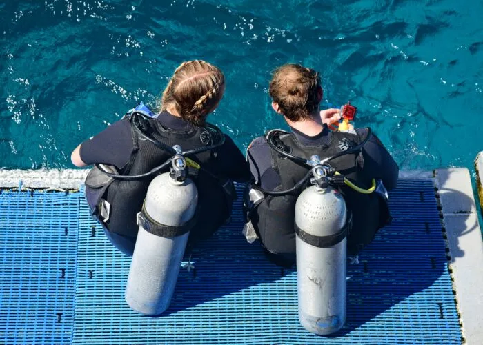 Deux plongeurs assis sur un ponton, équipement complet, vue mer