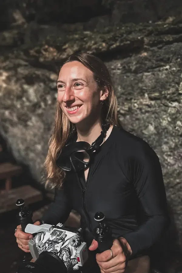 Plongeuse souriante tenant un détendeur dans un environnement rocheux sombre