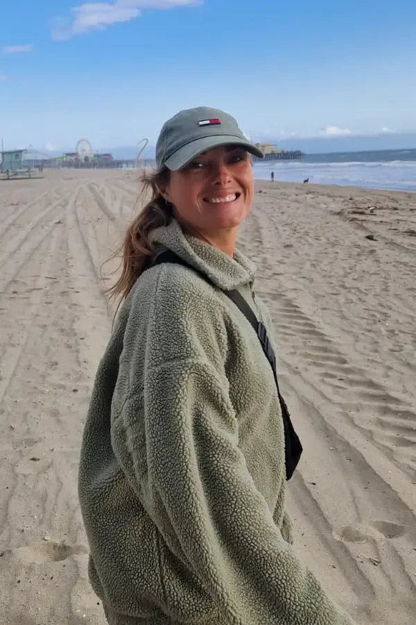 Jeune femme souriante sur une plage de sable, portant une casquette