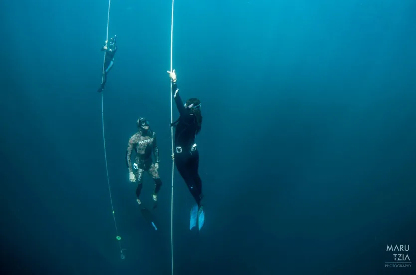 Trois apnéistes descendent le long d'un guide vertical dans l'eau bleue
