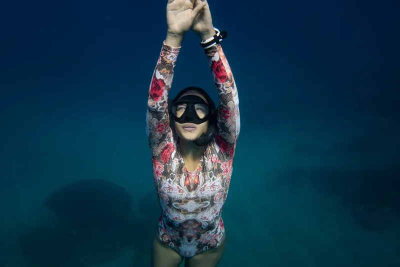 Apnée : une femme plonge, bras levés, dans une eau turquoise claire
