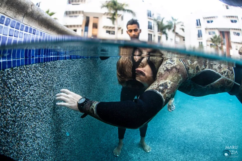 Plongeur en combinaison regarde vers la surface d'une piscine claire