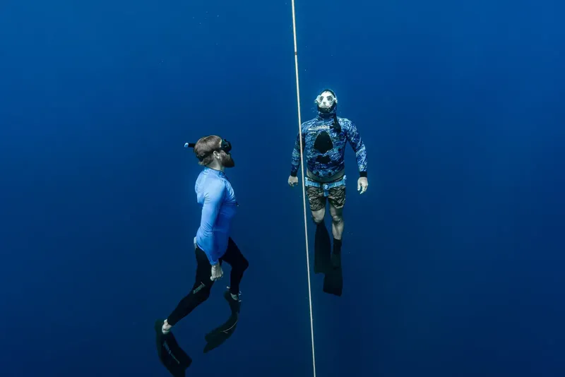 Deux apnéistes en combinaison descendent le long d'un câble bleu