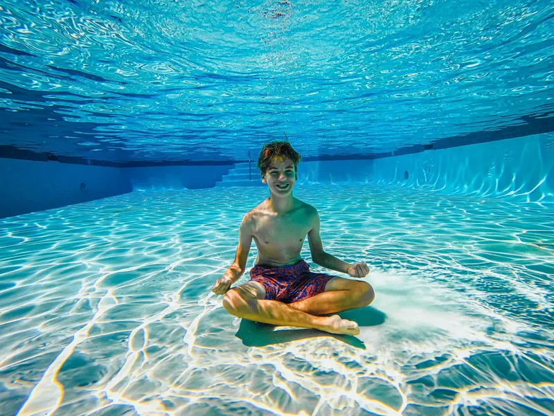 Jeune homme souriant en position de lotus sous l'eau dans une piscine