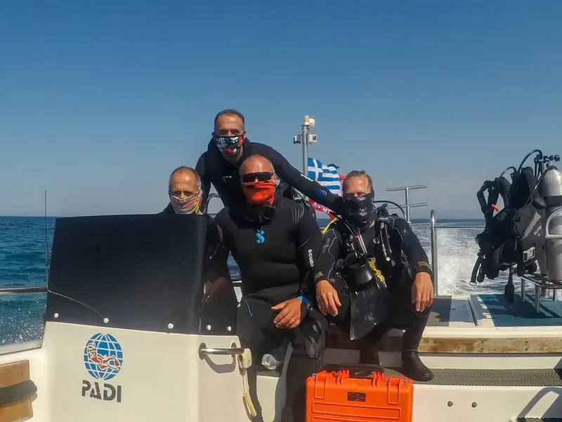 Trois plongeurs souriants avec masques et combinaisons sur un bateau
