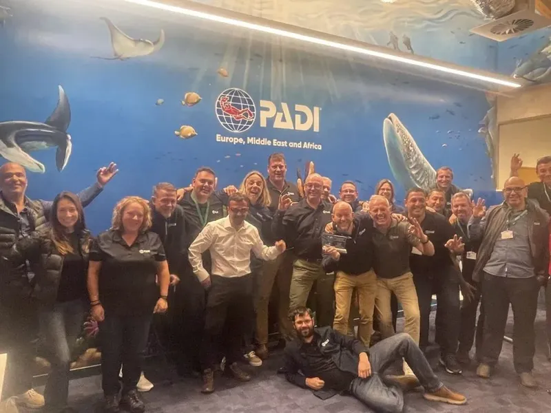 Groupe de personnes souriantes posant devant un mur avec le logo PADI