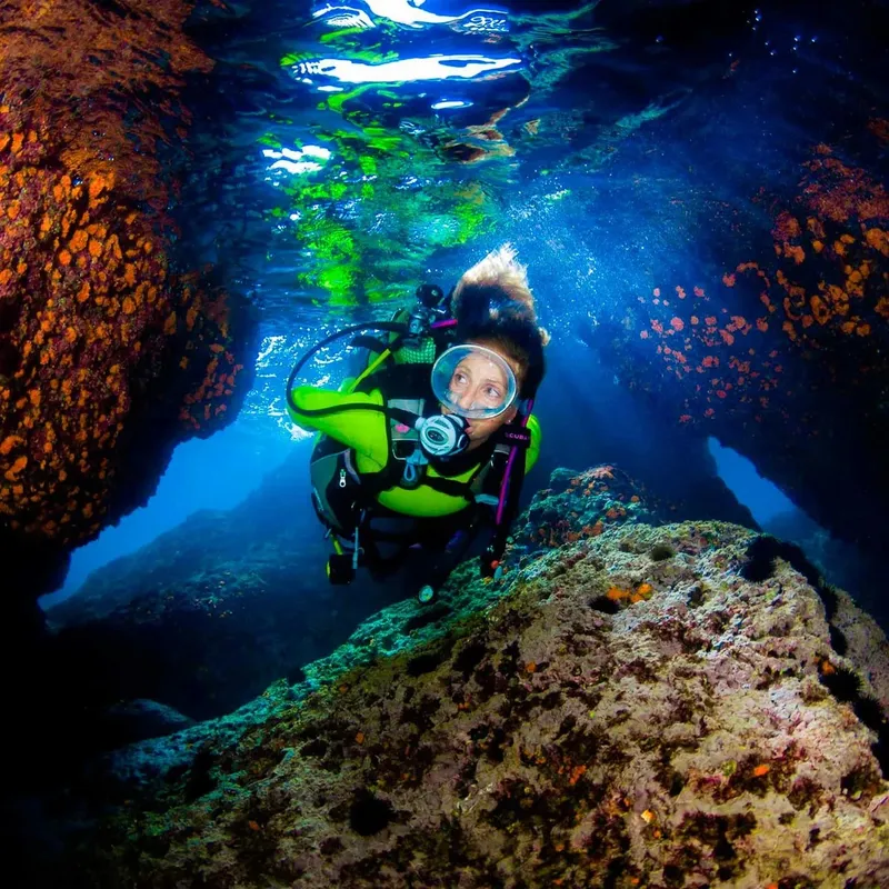 Plongeuse souriante explorant une grotte sous-marine rocheuse et lumineuse