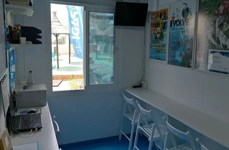 Bureau d'accueil avec ordinateur, imprimante, affiches de plongée et chaises