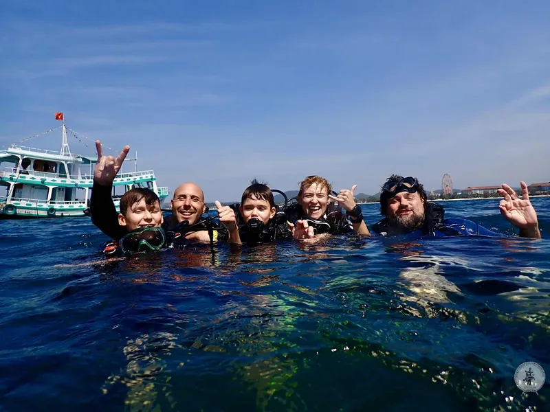 Cinq plongeurs souriants et équipés en mer, bateau en arrière-plan