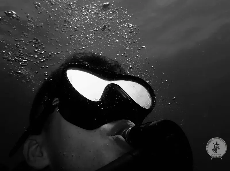 Plongeur avec masque noir, regard vers le haut, bulles et lumière diffuse