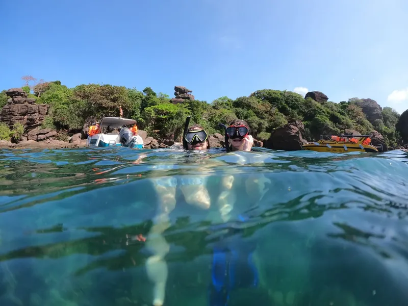 Deux plongeurs émergent, regardant un bateau au large d'une côte rocheuse