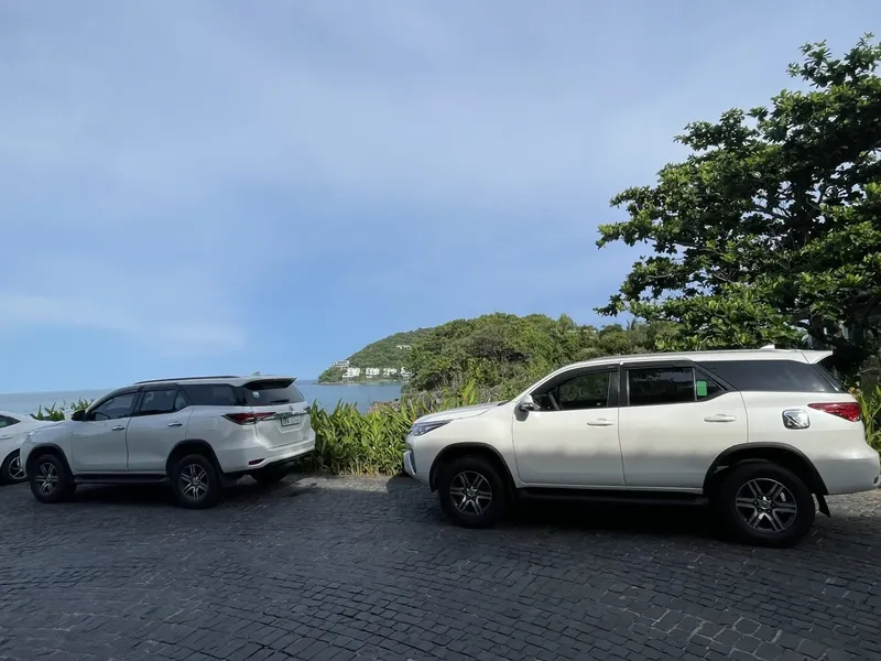 Parking avec des voitures blanches et vue sur la mer et végétation