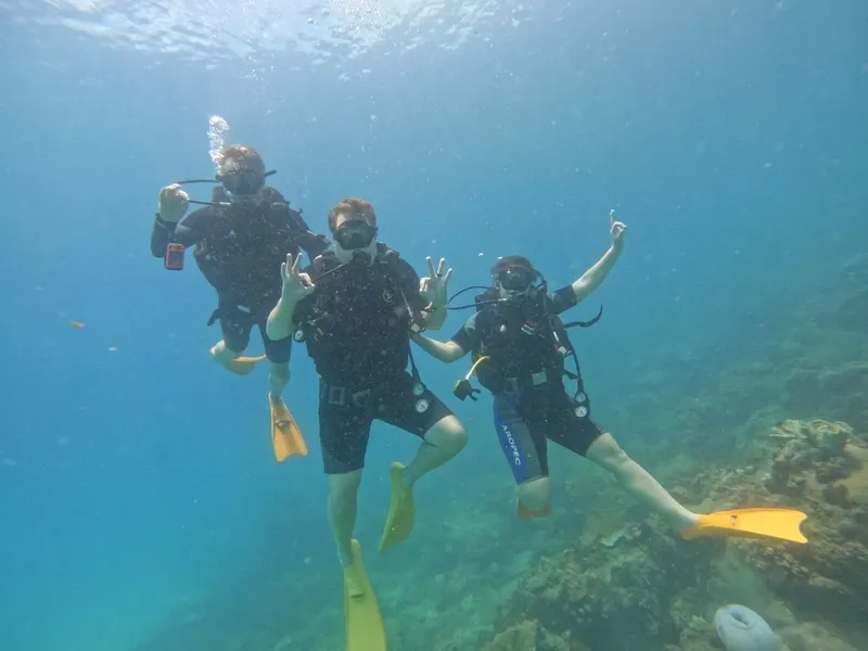 Trois plongeurs souriants font des signes de la main sous l'eau