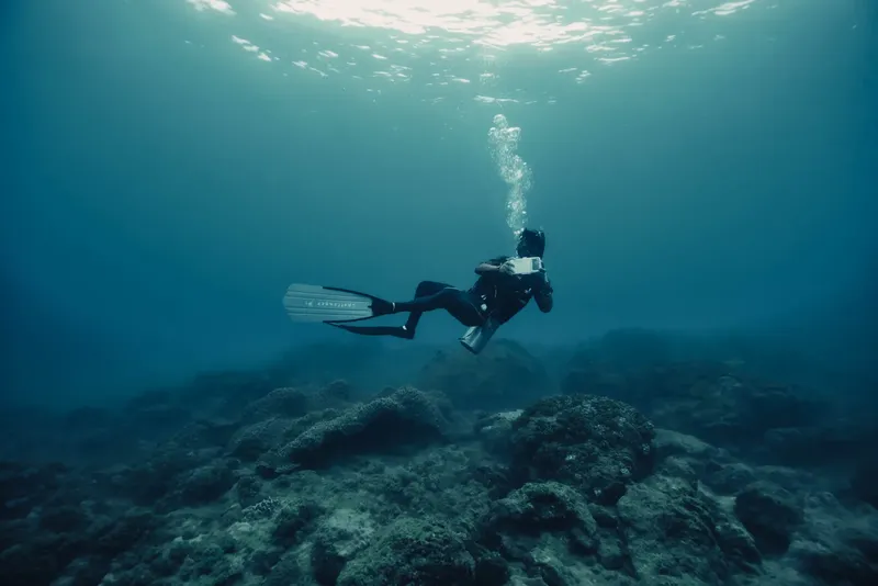 Plongeur en combinaison nageant dans une eau bleue au-dessus d'un fond rocheux