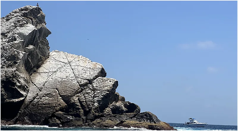 Rocher escarpé en bord de mer avec un bateau à l'horizon