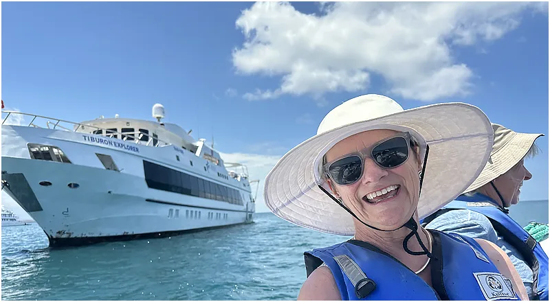 Femme souriante avec chapeau et gilet de sauvetage devant un bateau