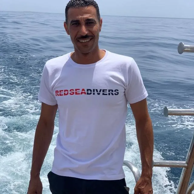 Homme souriant sur un bateau en mer, portant un t-shirt