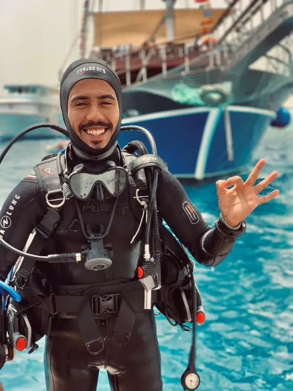 Plongeur souriant avec son équipement complet devant un bateau de plongée