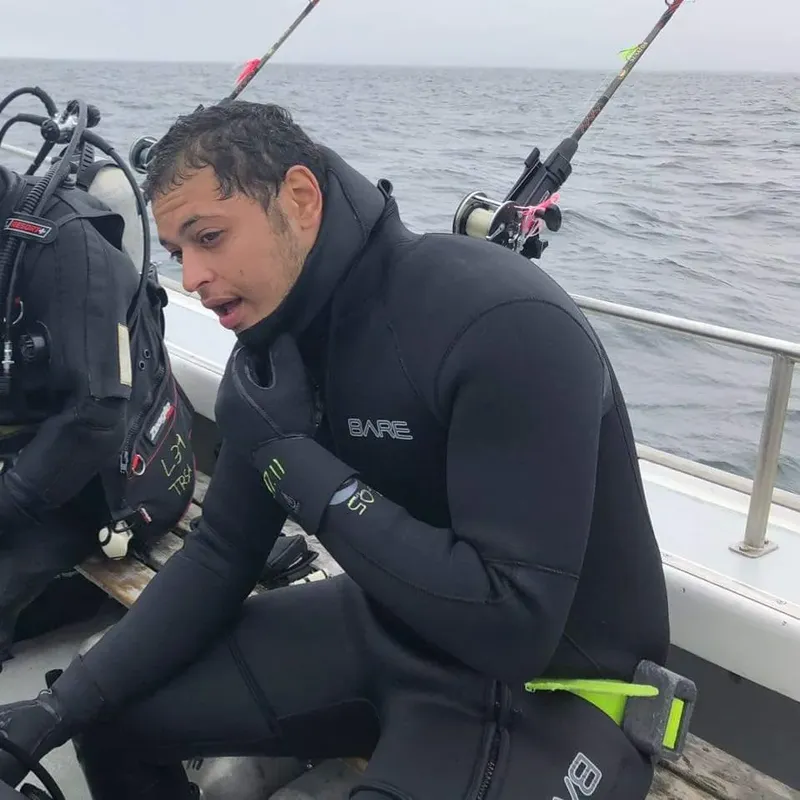 Plongeur en combinaison noire vérifie son équipement sur un bateau