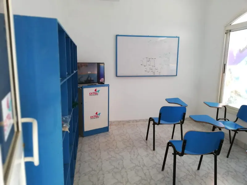 Salle de cours avec tableau blanc, chaises bleues et télévision