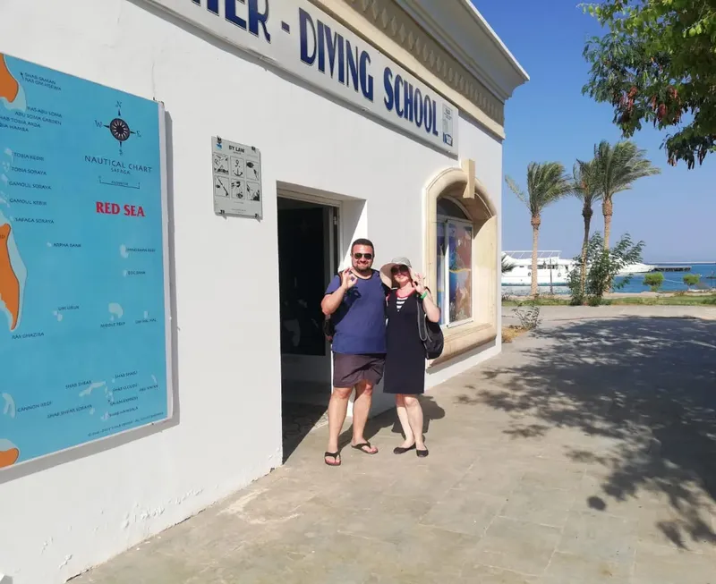 Deux personnes souriantes devant l'entrée d'une école de plongée