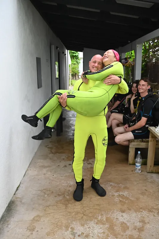 Deux plongeurs en combinaison jaune, un homme portant une femme souriante