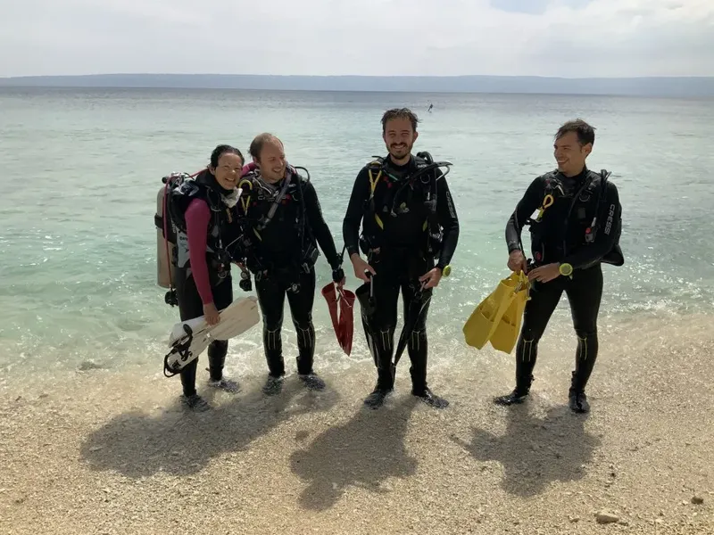 Quatre plongeurs en combinaison sur une plage de galets ensoleillée
