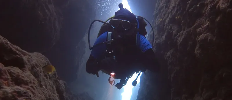 Plongeur explorant une fissure rocheuse sous-marine avec équipement complet