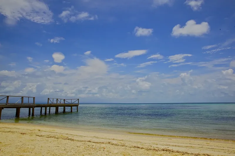 Plage de sable blanc, ponton en bois et ciel nuageux bleu