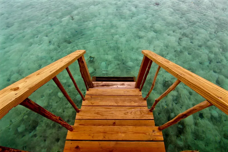 Escalier en bois descendant vers une eau turquoise claire et peu profonde