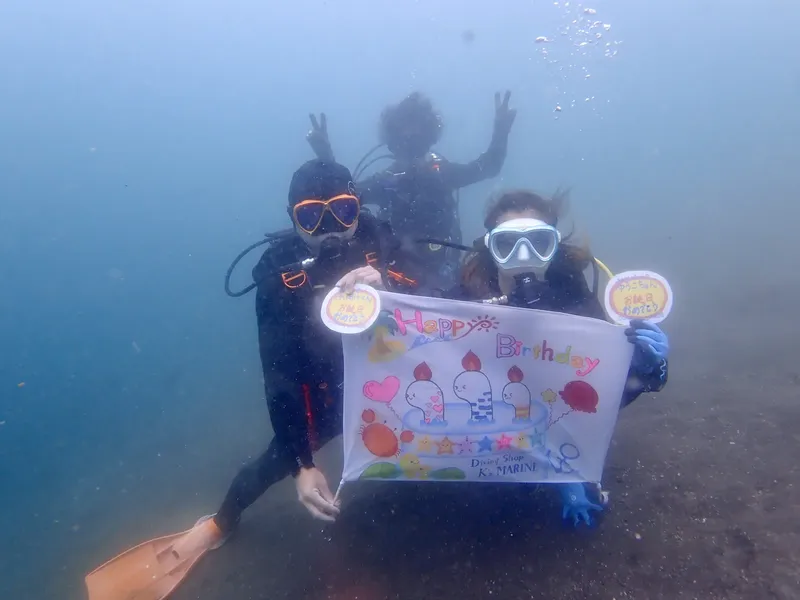 Deux plongeurs souriants tiennent une bannière joyeux anniversaire sous-marine