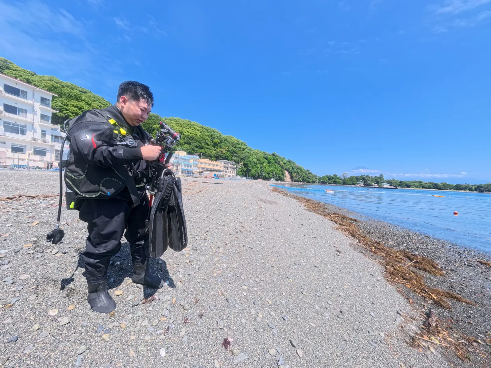 Plongeur en combinaison préparant son matériel sur une plage de galets