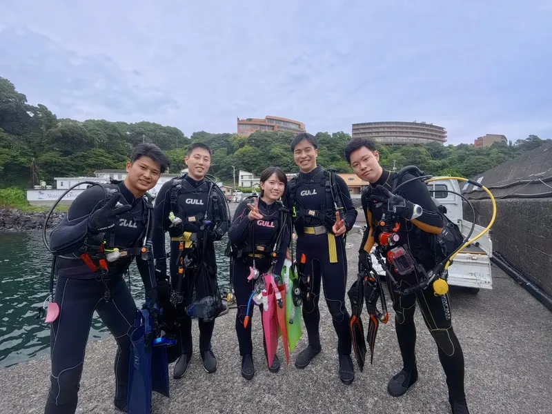 Groupe de plongeurs équipés souriant devant un quai et la mer