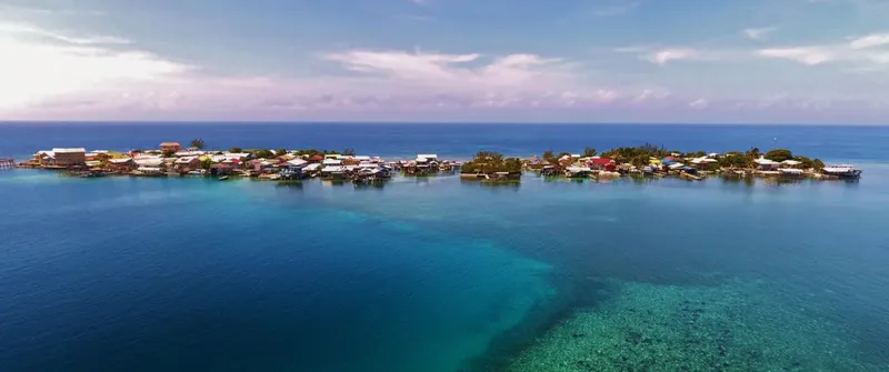 Village de palafittes sur l'eau turquoise, maisons colorées et végétation