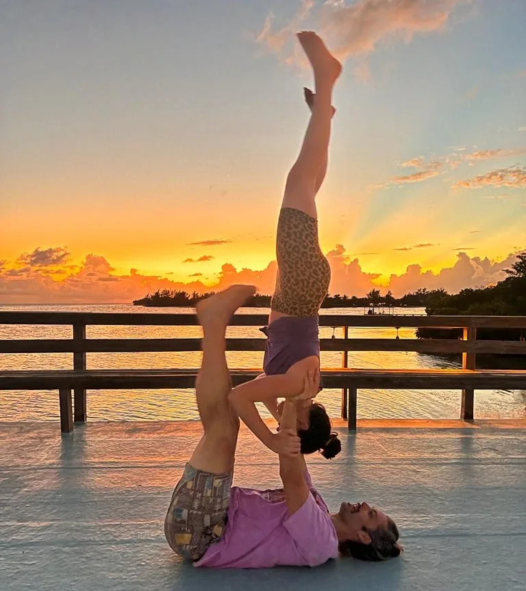 Deux personnes pratiquent l'acro-yoga sur un ponton au coucher du soleil