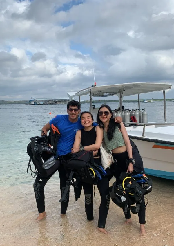 Trois plongeurs souriants avec leur équipement sur une plage