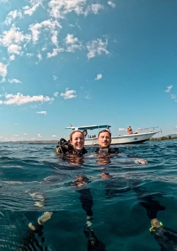 Deux plongeurs souriants émergent à la surface avec un bateau en arrière-plan