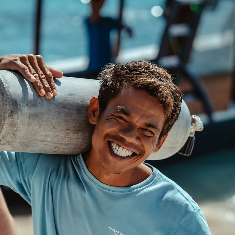 Homme souriant portant une bouteille de plongée sur son épaule