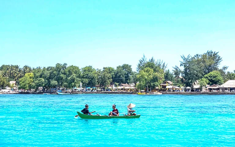 Trois personnes naviguent en pirogue sur une mer turquoise ensoleillée