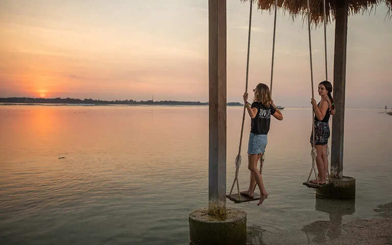 Deux jeunes femmes se balancent sur des balancelles au coucher du soleil